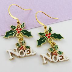 Christmas Charm Hook Earrings with Holly & Noel Message charms      Materials:     Earring Hooks - Brass   Charms - Alloy & Enamel      Approx. Total Earring Length: 40 mm Gold Earrings For New Year Holiday, Gold Earrings For Holiday And New Year, Gold Dangle Earrings For Christmas, Christmad Wreth Earrings, Christmas Bell Earrings, Green Dangle Christmas Jewelry, Holly Earrings, Christmas Festive Jewelry Charms, Brass Hooks