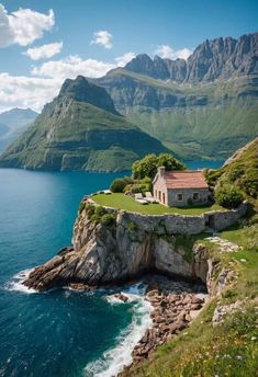 an island with a house on it in the middle of water and mountains behind it