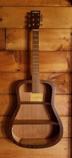 an acoustic guitar hanging on the wall in front of a wooden paneled wall with wood planks