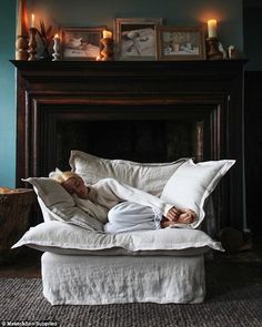 a baby laying on top of a white bed next to a fire place in a living room