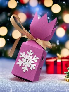 a purple gift box with a snowflake design on it and a christmas tree in the background