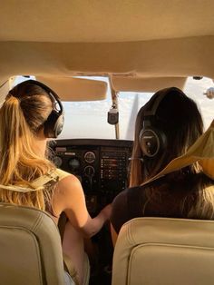 two women are sitting in the cockpit of an airplane with headphones on and one is wearing ear muffs