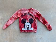 a red mickey mouse shirt laying on top of a cement floor