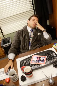 a man sitting at a desk in front of a computer keyboard and coffee mugs