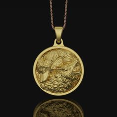 a gold necklace with a mountain scene in the center on a black background, it's reflection is shown