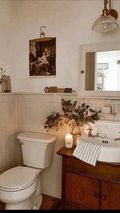 a white toilet sitting next to a wooden cabinet in a bathroom under a painting on the wall