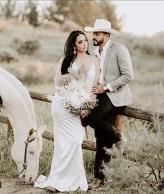 a bride and groom sitting on a fence next to a white horse with flowers in their hands