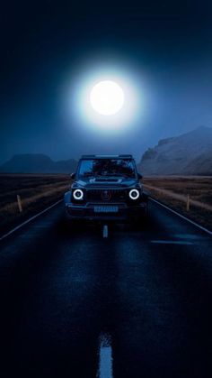 a car driving down the road at night under a full moon in the sky above