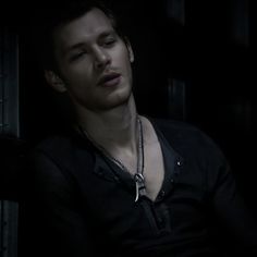 a young man is sitting in the dark with his hand on his chest and looking off into the distance