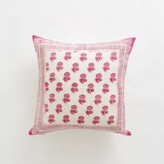 a pink and white pillow with red skulls on the front, sitting against a white wall