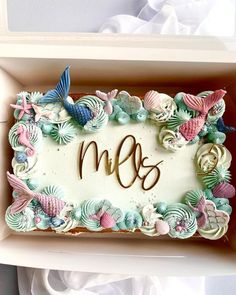 a decorated cake in a box with the letter m and seashells on it