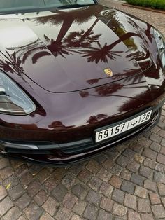 a maroon sports car parked in front of a palm tree