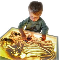 a young boy playing with toys in front of a lit up table top that has an image of a skeleton on it