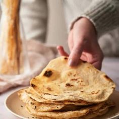 a stack of flatbreads on a plate with a hand reaching for the top