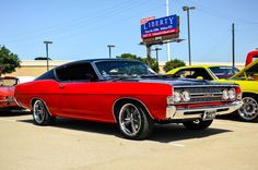 an old red car parked in a parking lot next to other classic cars and trucks