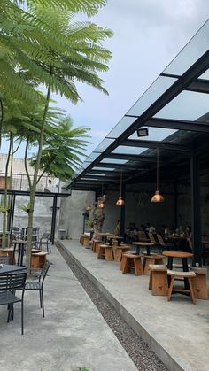 an outdoor dining area with wooden tables and chairs under a metal awning next to palm trees