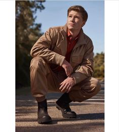 a man squatting down on the ground with his hands in his pockets and shoes