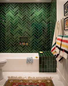 a bathroom with green tiles on the wall and rug in the bathtub, toilet and sink