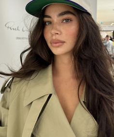 a woman with long brown hair wearing a green hat and trench coat at an event