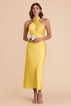 a woman in a yellow dress holding a white flower and looking at the camera with her hands on her hips