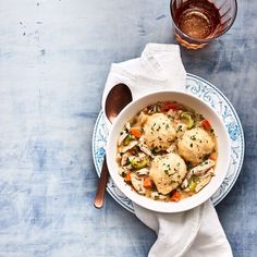 a bowl filled with chicken and vegetables next to a glass of wine on top of a table