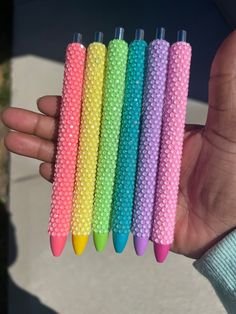 a person holding five different colored pens in their hand