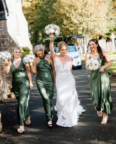 three bridesmaids walking down the street with their bouquets in hand and one holding her dress