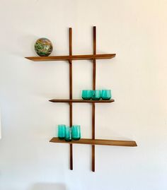 three wooden shelves with teal glass cups on them and a vase in the corner