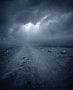 an empty road in the middle of nowhere under a dark sky with storm clouds above