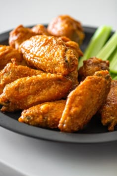 chicken wings and celery on a black plate with white table cloth in the background