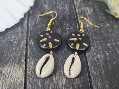 "These gorgeous dangle earrings feature genuine off-white sliced moneta cowrie shells dangling beneath 20mm round carved black and gold acrylic beads an etched Afrocentric abstract pattern. Aching for acrylics? Check out the rest of my acrylic jewelry here: https://etsy.me/2IadiWZ Throughout Africa and the Americas, cowrie shells have historically been viewed as symbols of womanhood, fertility, and prosperity. Check out my other cowrie shell jewelry here: https://etsy.me/2VQS0r0 These earrings m Cowrie Shell Earrings For Gifts, Black Dangle Jewelry For Beach, Artisan Black Jewelry For The Beach, Black Shell Jewelry For Gifts, Black Shell Jewelry Gift, Black Shell Jewelry As A Gift, Unique Black Beach Jewelry, Handmade Black Jewelry For Vacation, Black Shell Bohemian Jewelry