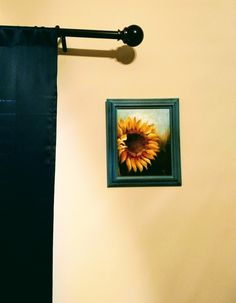 a sunflower is hanging on the wall next to a blue framed photograph with a black curtain