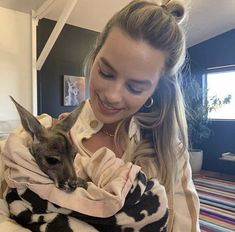 a woman holding a baby kangaroo in her arms and smiling at the camera while wearing a cow print sweater