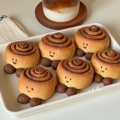 there are many rolls with faces on them in a tray next to a cup of coffee