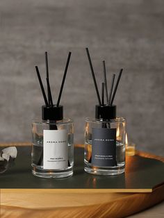 two candles with labels on them sitting on a table next to a bottle of perfume