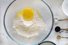 ingredients in a bowl on a white countertop including eggs, flour and measuring spoons