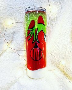 a red and green tumbler cup sitting on top of a white blanket with string lights