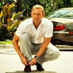 a man squatting down on the ground with his shoes in front of him and cars behind him