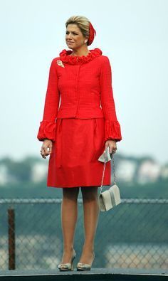 a woman in a red dress standing on top of a roof with her handbag