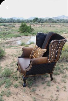 an old chair with some pillows on it in the middle of a dirt field and bushes