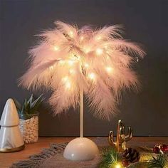 a white christmas tree decorated with lights and feathers on a table next to other decorations