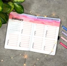 an open planner sitting on top of a table next to some pens and a potted plant