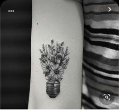 a black and white photo of a vase with flowers on the side of a woman's arm