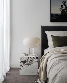 a bedroom with a marble nightstand next to a white bed and painting on the wall