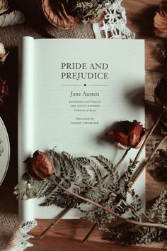 an open book sitting on top of a wooden table next to dried flowers and leaves