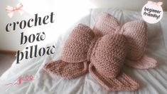 the crochet bow pillow is made from pink yarn and sits on a bed