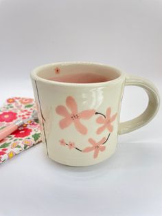 a white cup with pink flowers on it next to a notebook