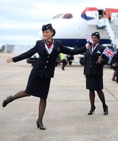 two women dressed in british airline uniforms are dancing on the tarmac