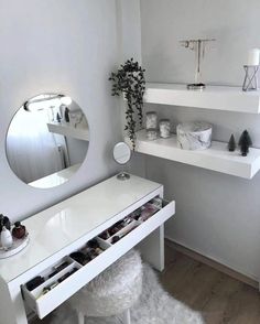 a white dressing table with drawers under a round mirror and shelves above it, filled with cosmetics