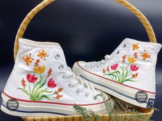 a pair of white sneakers with flowers painted on them sitting in a basket next to plants